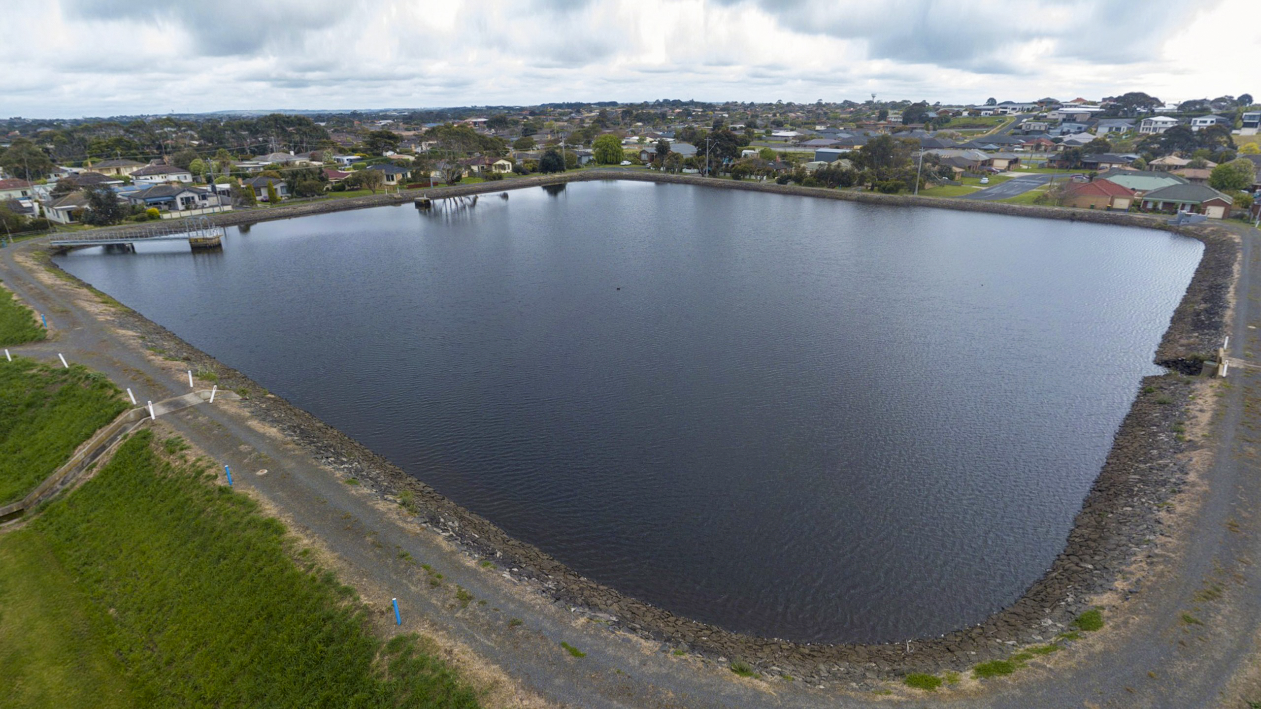 Before: Birds eye view of Brierly Basin water storage dam full of water, with residential housing in the background.